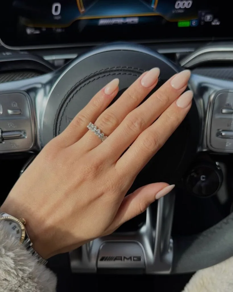 Almond-shaped nude old money nails, milky and glossy, styled with diamond ring in a car.
