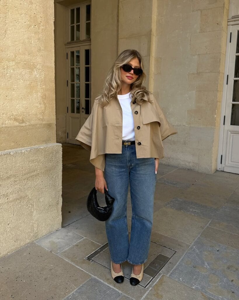 Woman in cropped trench coat, jeans, white tee, and sunglasses in a city setting