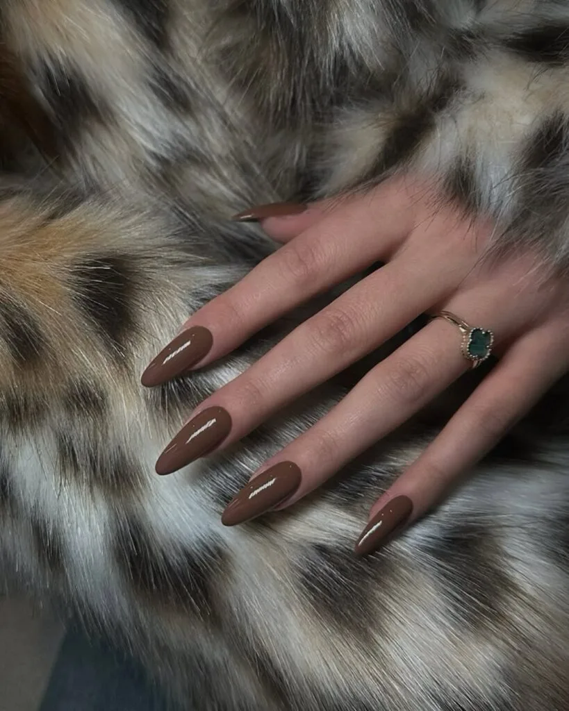 Almond-shaped espresso old money nails, glossy, styled with gold emerald ring and faux fur coat.