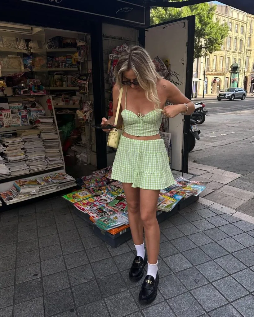 Woman in green gingham crop top and skirt with black loafers, white socks; loafers outfit, playful summer look.