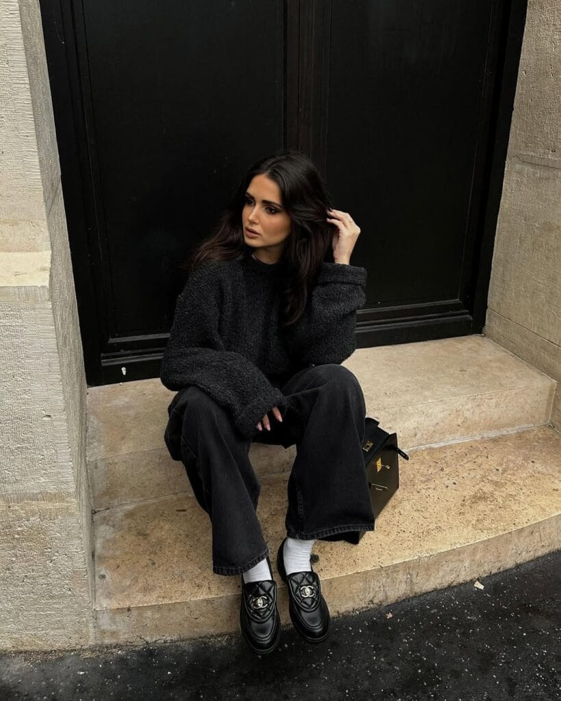 Woman in black sweater, wide-leg trousers, Chanel loafers, white socks, sitting on steps; textured loafers outfit.