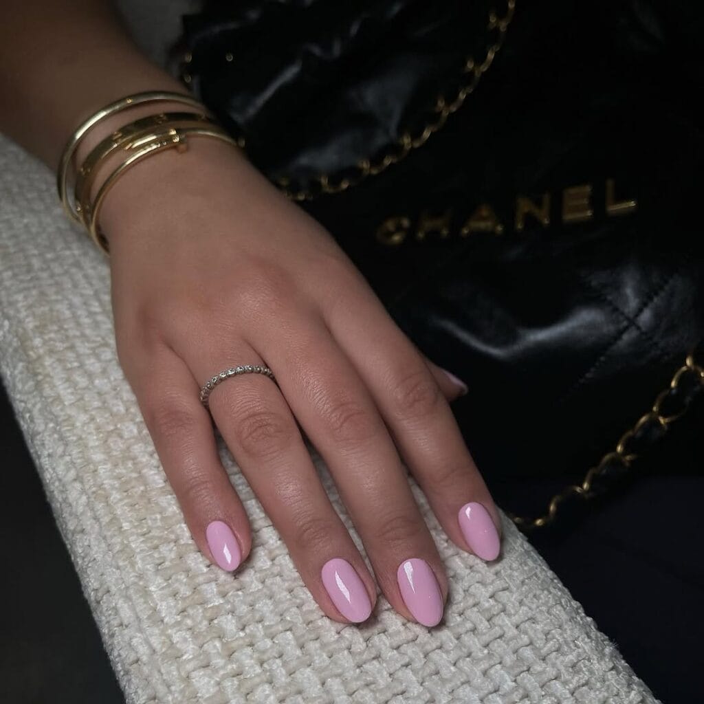 Glossy pink old money nails with gold bracelets, styled with a Chanel bag for chic, luxe effect.
